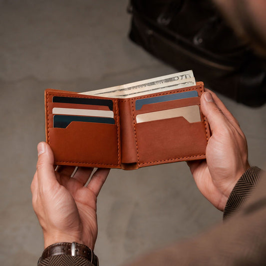 Toscano | A person holds an open leather bifold wallet with multiple card slots and cash