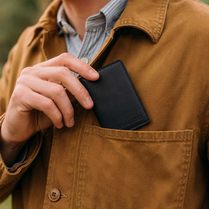 Nero | A close-up of a model sliding a leather card holder into their shirt pocket